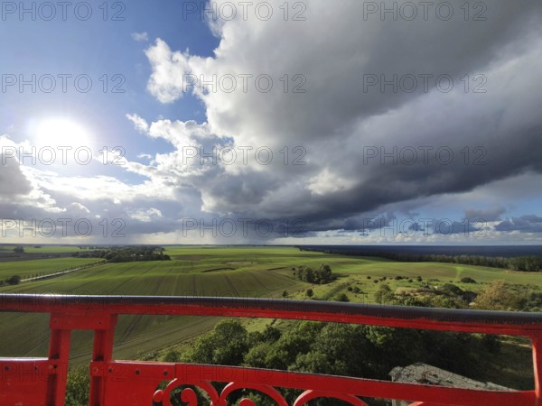 View of green fields under dramatic sky with dark clouds, red railings in the foreground and sunshine, Cape Arkona lighthouse, Rügen