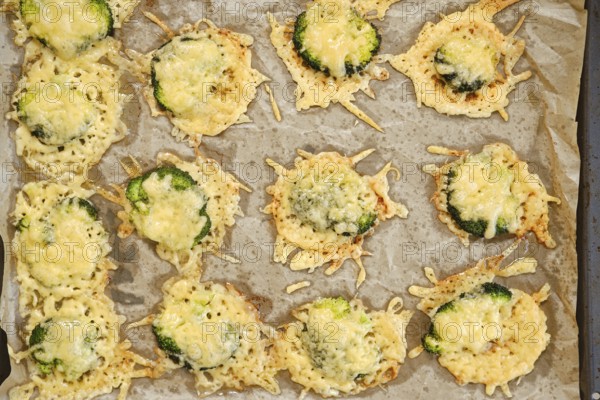 Broccoli pieces are smashed and spread on a baking sheet. They are topped with cheese and placed in an oven