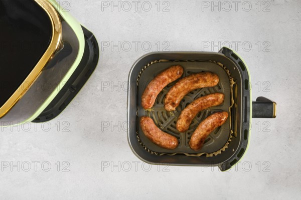Natural casing sausages in an air fryer, being cooked at high heat. This activity shows the process of preparing a meal in a modern kitchen setting. The sausages are brown and ready