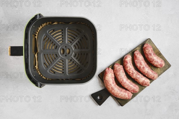 Fresh natural casing sausages on a cutting board beside an air fryer basket. The sausages are ready to be cooked for a meal. Preparation takes place in a kitchen setting