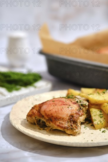 A plate holds a crispy chicken thigh next to golden roasted potatoes. Fresh green herbs are sprinkled on the food