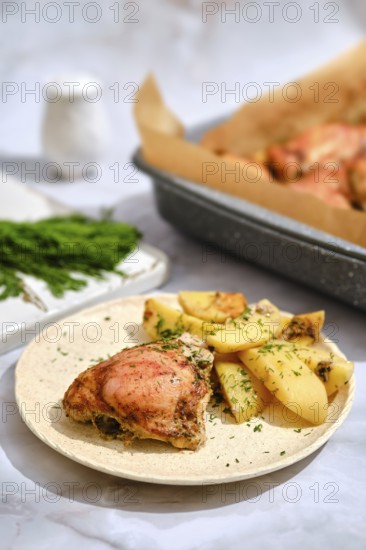 Roasted chicken and potato wedges. Baking tray is seen in the background with more chicken. The kitchen is bright and inviting