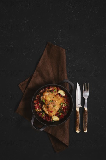 A warm bowl holds a tasty meal featuring chicken with lingonberry placed on a brown cloth. A knife and fork rest beside the bowl, ready for someone to enjoy the food