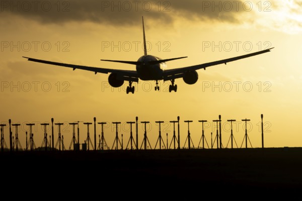 Boeing 777 commercial passenger jet aircraft in flight on approach to land over runway lights silhouette at sunset at London Stansted airport, Essex, England, United Kingdom