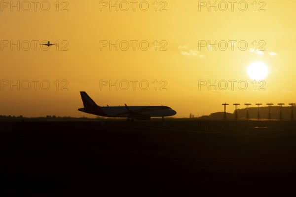 Airbus commercial passenger airliner jet aircraft taking off in flight with another plane on the taxiway at sunset at London Stansted airport, Essex, England, United Kingdom
