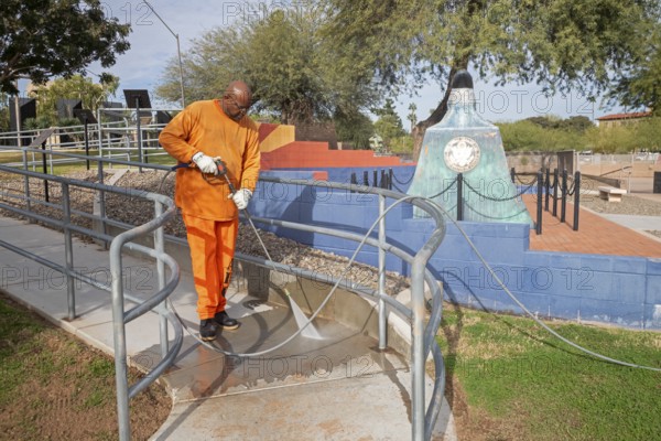 Phoenix, Arizona - A prisoner cleans a sidewalk in Wesley Bolin Memorial Plaza, a public park next to the Arizona State Capitol complex. The Arizona Department of Corrections puts thousands of prisoners to work every day on a varieyt of projects
