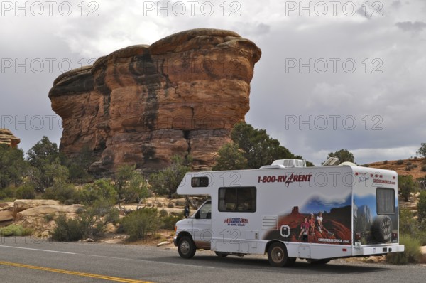Motorhome standing on a road in front of a distinctive rock formation under a cloudy sky, Canyonlands National Park, Utah, USA