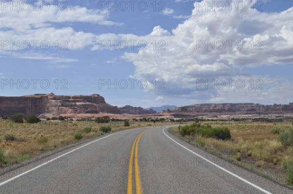 A road leads through vast desert landscape with impressive rock formations and cloudy skies, Canyonlands National Park, Utah, USA