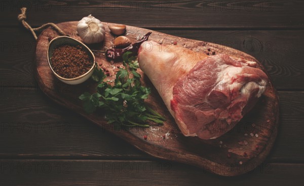 Raw pork knuckle, on a wooden chopping board, with spices, close-up, top view, no people