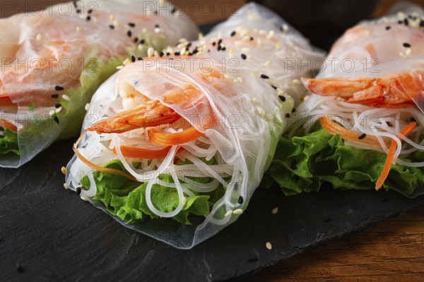 Shrimp rice paper rolls on a black plate with fresh vegetables and sesame seeds