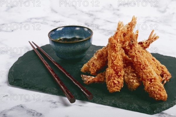Shrimp in tempura, deep fried, on black slate, with sauce, light marble table, no people