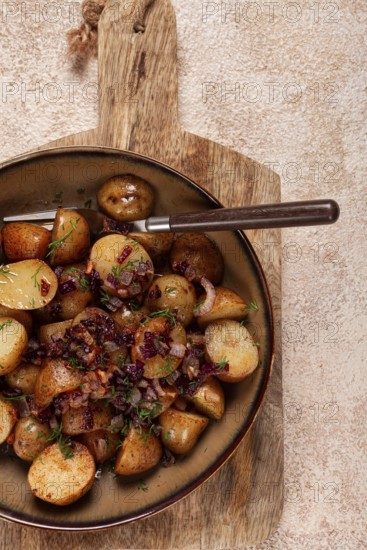 Succulent golden-brown roasted potatoes are served with sweet caramelized onions, garnished with fresh herbs, all beautifully arranged on a rustic wooden board in a warm kitchen
