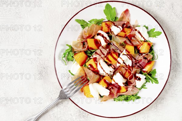 Salad with slices of ripe melon, prosciutto, mozzarella and fresh arugula, decorated with balsamic glaze