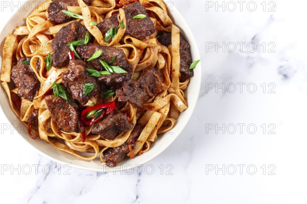 Udon noodles with Mongolian beef, green onions and vegetables, in a white plate, on a light background, homemade, no people