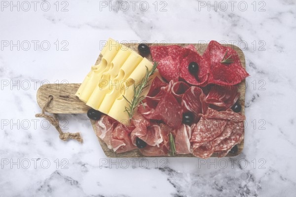 Assorted meat, appetizer, prosciutto, salami and ham, with maasdam cheese and olives, on a wooden board, breakfast, top view, close-up, no people