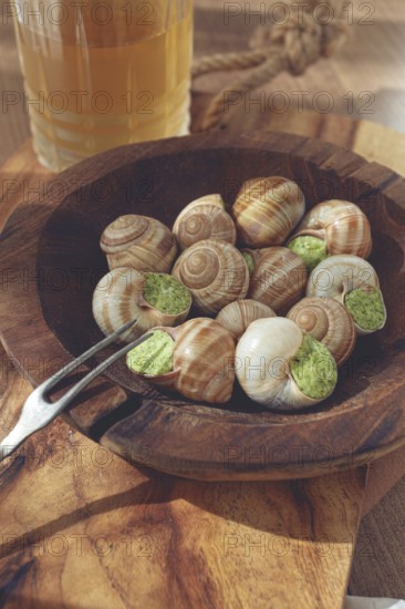 Snails cooked with herb oil on a wooden plate, served with white wine, natural light, no people