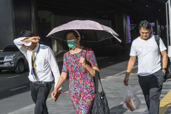 Bangkok, Thailand. March 25th 2025. People shield their faces from the bright sun and wear face masks during the intense summer heat and harsh climate in the Thai capital, Bangkok, Thailand