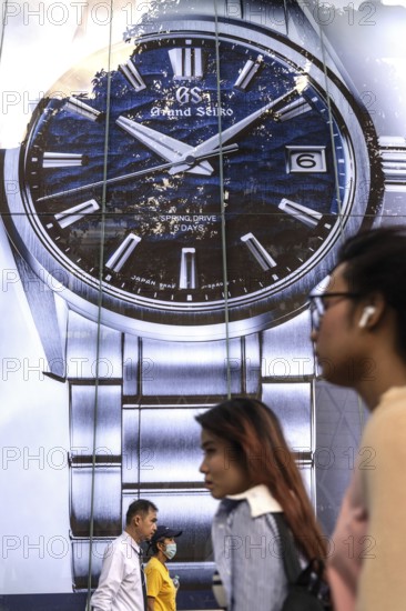 Bangkok, Thailand. March 25th 2025. A busy shopping street with pedestrians passing a large advertisement for luxury watch brand Grand Seiko in Siam Square district of Bangkok, Thailand