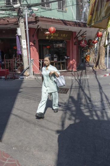 Bangkok, Thailand. March 25th 2025. A local women walking past Chinese restaurants and the shadows of overhead electrical wires in the Chinatown district of the Bangkok, capital of Thailand