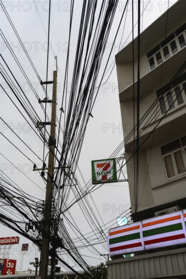 A mess of tangled wires and cables attached to a telegraph pole outside a 7 Eleven store in Bangkok, capital city of Thailand