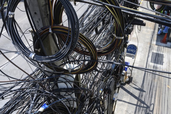 Bangkok, Thailand. March 4th 2025. A tangled mess of cables and wires used for phone and internet connections hanging from a pole in the street in central Bangkok, Thailand