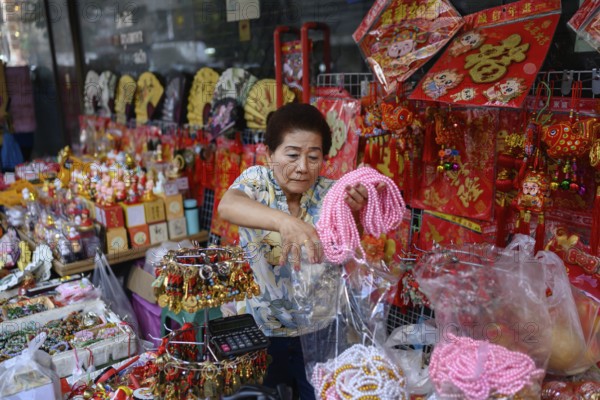 Bangkok, Thailand. February 18th 2025. A woman selling Chinese souvenirs and gifts from a street side stall along Yaowarat Road, Chinatown, Bangkok, Thailand