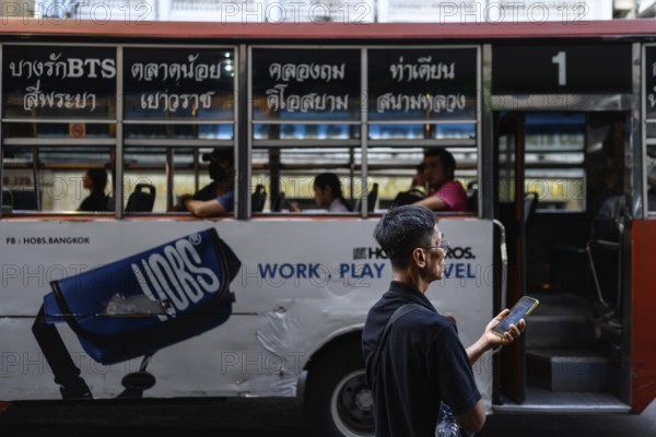 Bangkok, Thailand. February 18th 2025. A local man with a mobile phone waiting for a bus in Yaowarat Road, Chinatown, Bangkok, Thailand