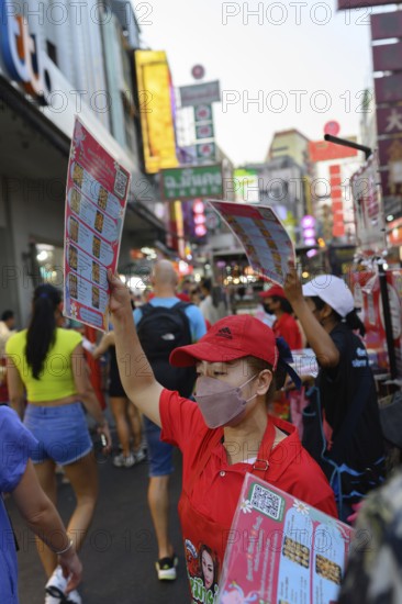Bangkok, Thailand. February 18th 2025. Restaurant waitresses wave menus to attract customers in Yaowarat Road, Chinatown, Bangkok, Thailand