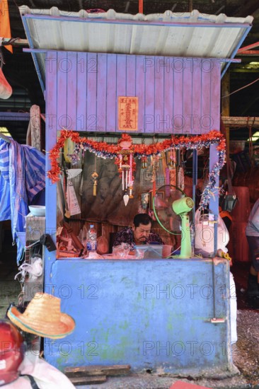 Bangkok, Thailand. February 19th 2025. A worker sits inside a colourful booth at the Khlong Toei Market, Bangkok, Thailand, Asia