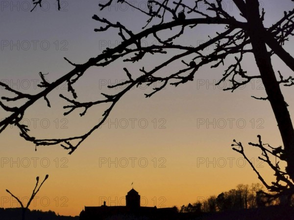 Branches in the foreground against a colorful sunset sky with the silhouette of Rosenberg Fortress on the horizon, Kronach, Frankenwald nature park Park