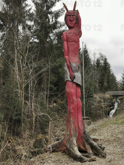 A red wooden sculpture at the entrance to Höllental in the shape of a devil looms in the forest, Frankenwald nature park Park