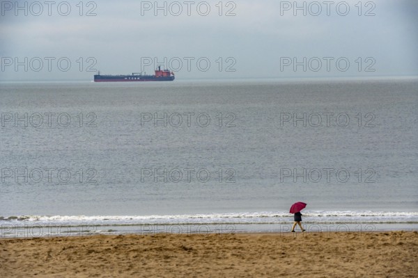 Winter break, on Zeedijk-Knokke, beach promenade in Knokke-Heist, beach walkers with umbrella when it rains, dreary winter day, freighter on the North Sea, Belgium