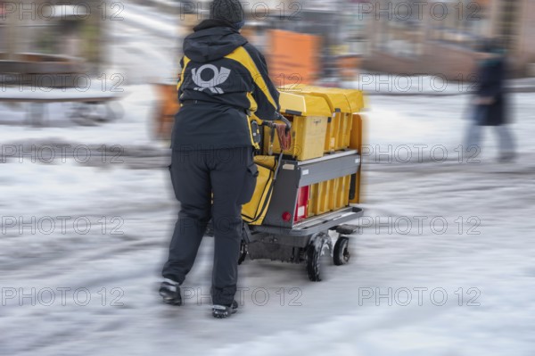 Movement, postman walking with loaded handcart on a wintry road in the city, Nuremberg, Middle Franconia, Bavaria, Germany