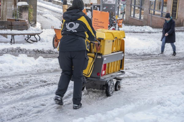Postman walking with loaded handcart on a wintry road in the city, Nuremberg, Middle Franconia, Bavaria, Germany