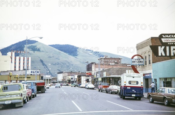 Vehicles on road Main Street in town downtown shopping area of Missoula, Montana, USA 1977 view to Mount Sentinel and Mount Jumbo