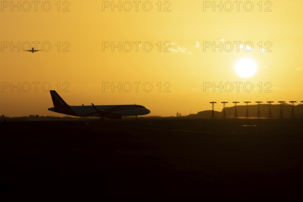 Airbus commercial passenger airliner jet aircraft taking off in flight with another plane on the taxiway at sunset at London Stansted airport, Essex, England, United Kingdom