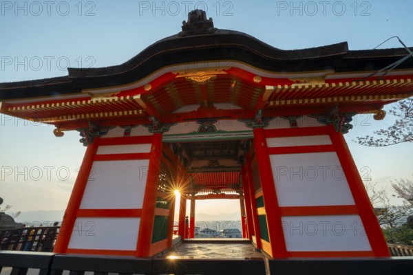 Sunset over the city with sun stars, view through the red Nishimon Gate, Kiyomizu-dera Temple, in the evening light, Buddhist temple complex, Higashiyama, Kyoto