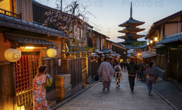Japanese woman and men wearing kimono in an alley, Yasaka dori historic alleyway in the old town with traditional Japanese houses, five-story Yasaka pagoda of the Buddhist Hokanji Temple, evening mood, Kyoto, Japan