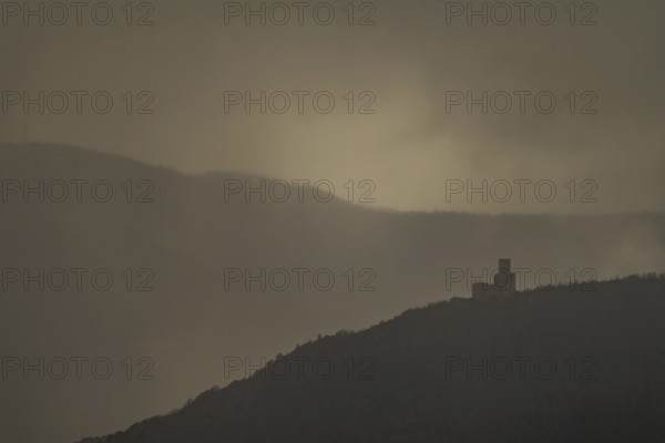 The structure is on a mountain. The sky is cloudy and sunlight is shining in the distance. The scenery shows a dark and mysterious atmosphere. Bas Rhin, Alsace, France