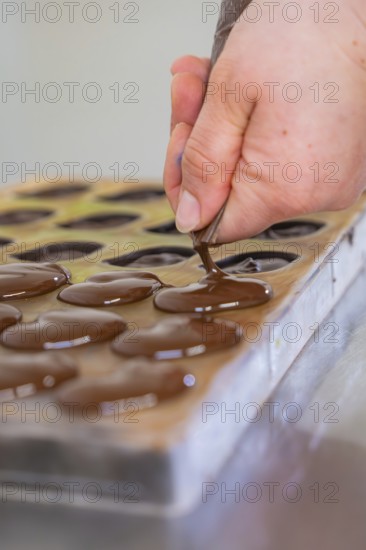 Hand fills chocolate into a mold on a table with a piping bag, vegan chocolates production, Haselstaller Hof, Gechingen, Germany