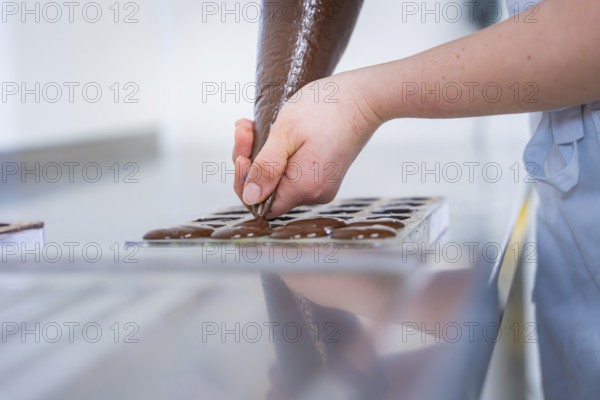 Chocolate is pressed into a chocolate mold by one hand, vegan chocolates production, Haselstaller Hof, Gechingen, Germany