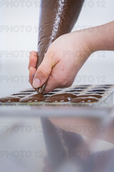 A hand injects chocolate into a mold to produce chocolates, vegan chocolates production, Haselstaller Hof, Gechingen, Germany