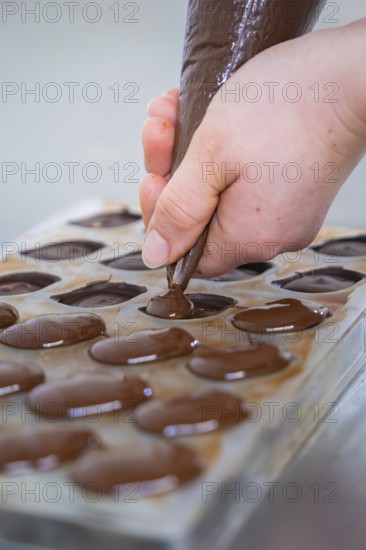 Close-up of a hand filling chocolate mold with liquid chocolate, vegan chocolates production, Haselstaller Hof, Gechingen, Germany