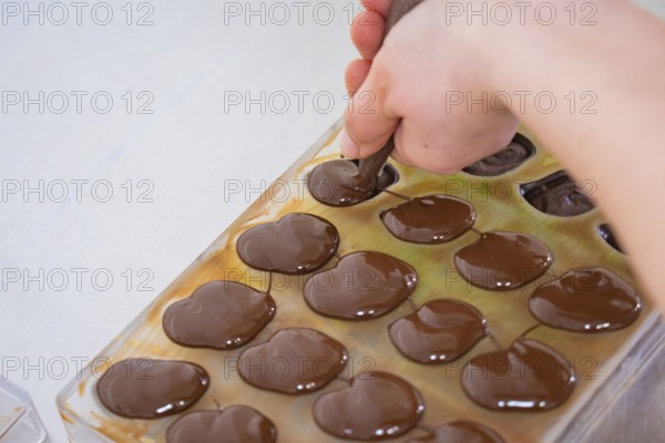 Hand with piping bag fills liquid chocolate in chocolate shape on a table, vegan chocolates production, Haselstaller Hof, Gechingen, Germany