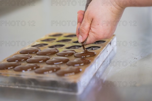 Hand fills chocolate into a chocolate mold lying on a table, vegan chocolates production, Haselstaller Hof, Gechingen, Germany