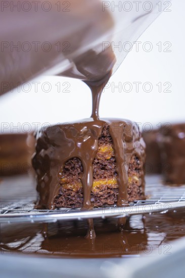 Chocolate coating is poured onto a small cake that is placed on a grid, Vegan Tartchen Production, Haselstaller Hof, Gechingen, Germany