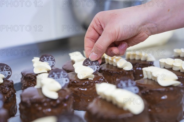 Small chocolate cakes are decorated with café logo and white chocolate, Vegan Tartchen Production, Haselstaller Hof, Gechingen, Germany