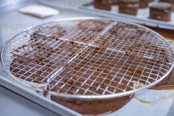 A metal grid with rotating chocolate grids, kitchen appliances in the background, vegan cake production, Haselstaller Hof, Gechingen, Germany
