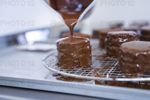 A pastry covered with liquid chocolate drips on a grid in a baking quality kitchen, vegan cake production, Haselstaller Hof, Gechingen, Germany