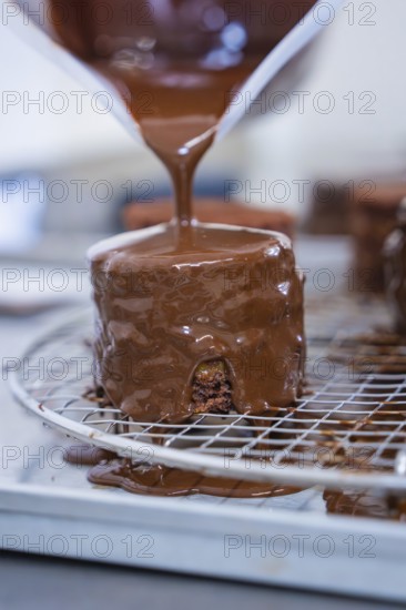 A small pastry is glazed with liquid chocolate and drips off a grid, Vegan Tart Production, Haselstaller Hof, Gechingen, Germany